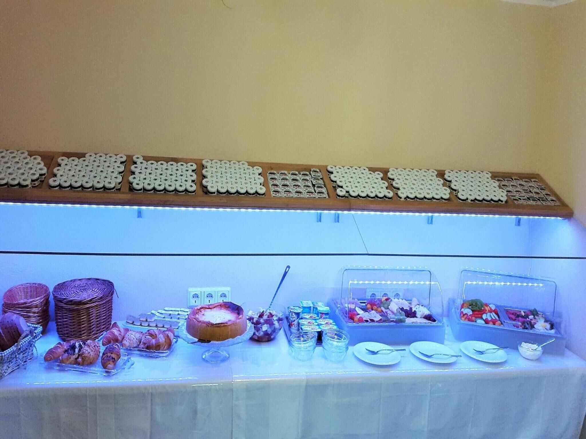 Une table de buffet garnie de divers plats, avec une présentation de pains ou de viennoiseries au-dessus.