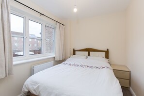 Un dormitorio con una cama individual, una mesita de noche, una ventana con cortinas y vistas a edificios.