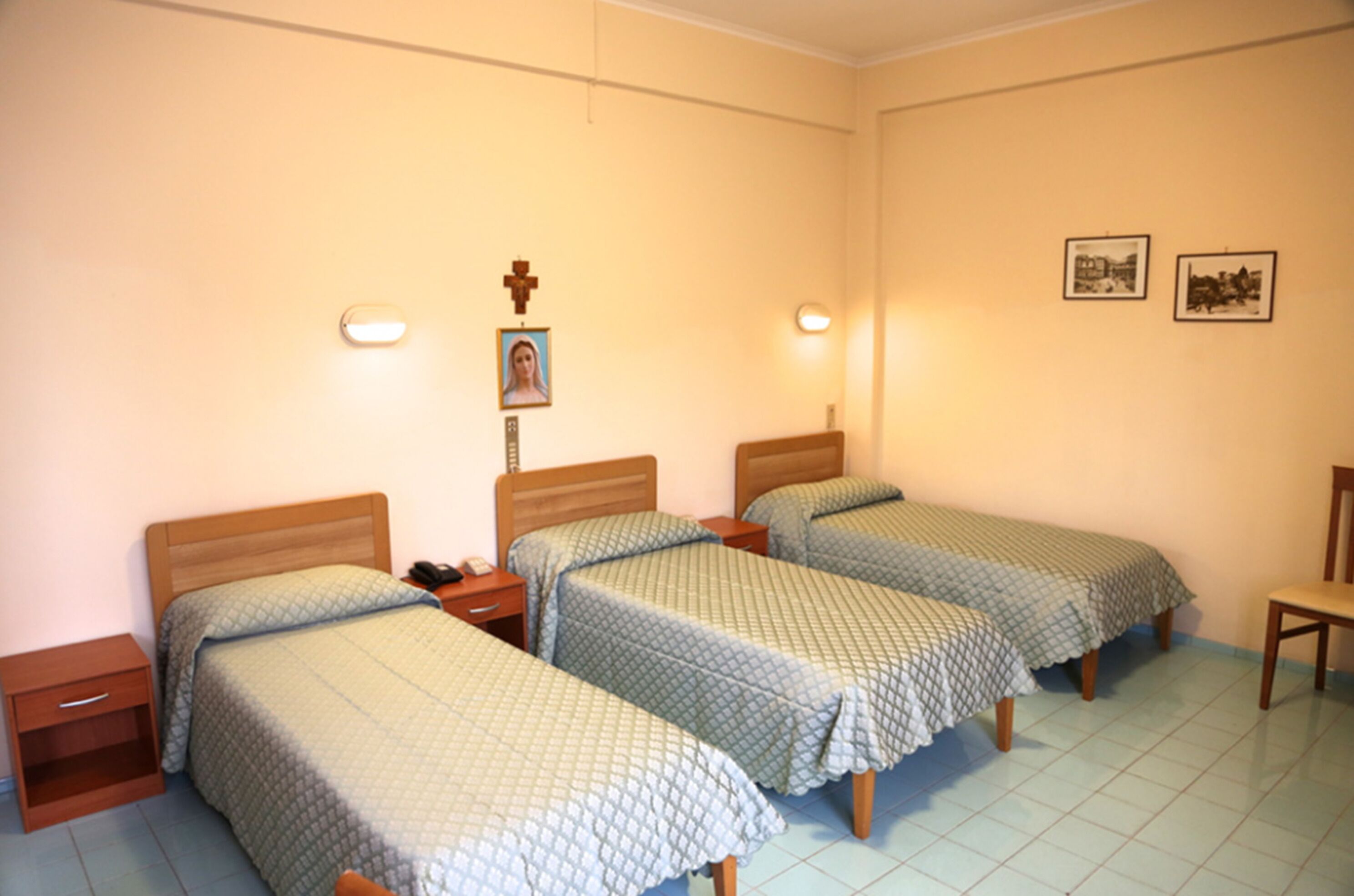 A room with three single beds, a wooden nightstand, a chair, and two wall-mounted lights.
