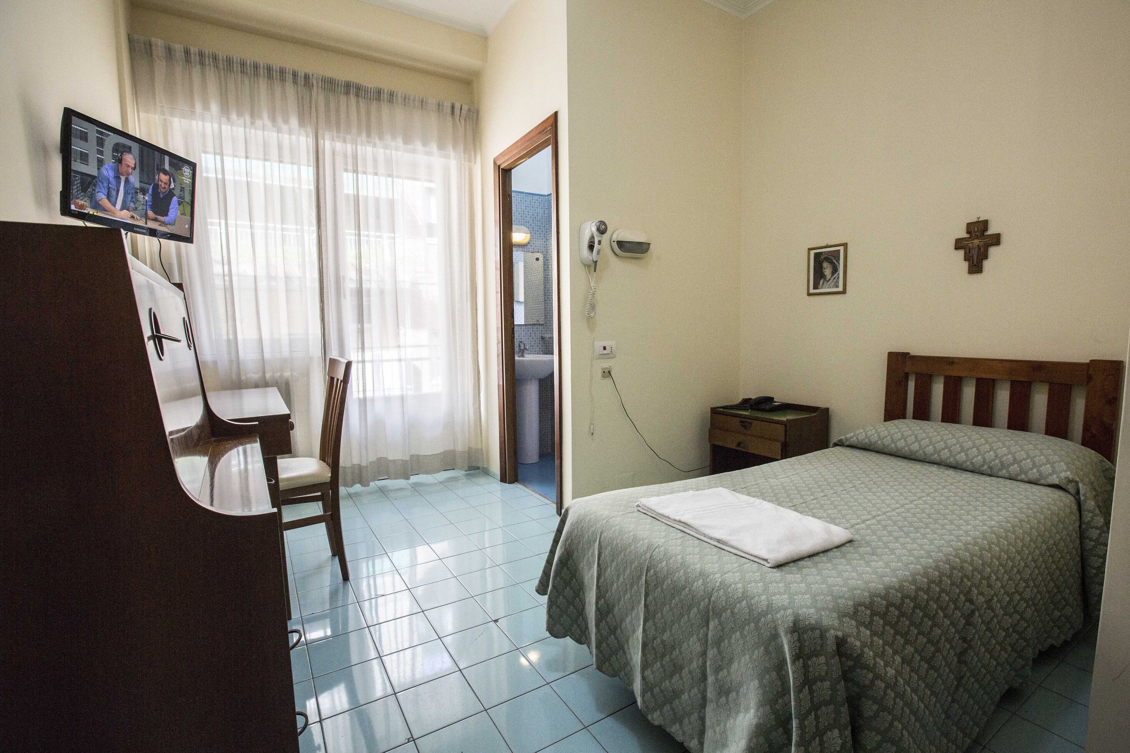 A hotel room with a bed, a desk with a chair, a television, and a bathroom visible through an open door.
