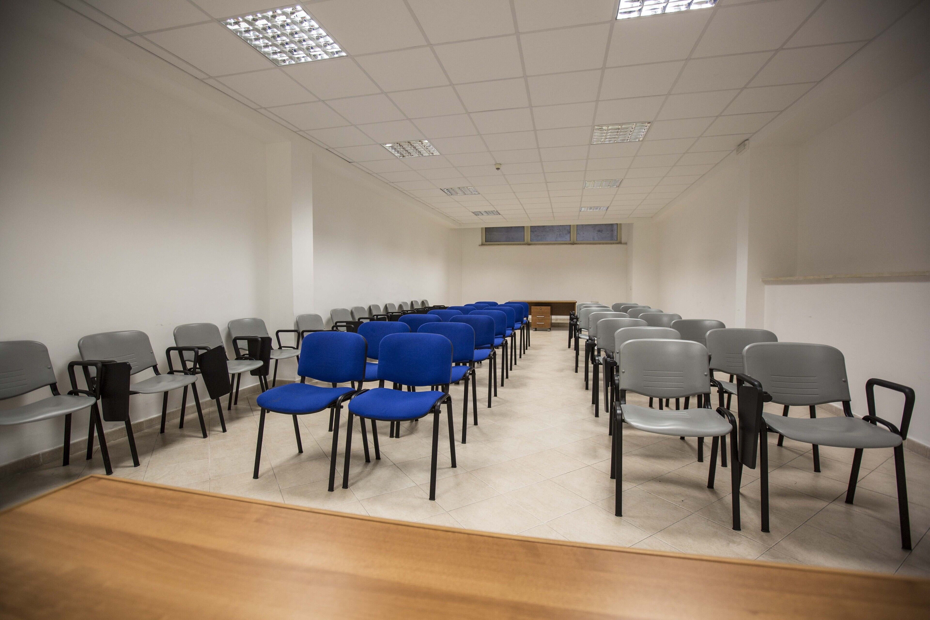 A conference room with rows of chairs, a wooden floor, and a white ceiling with lights.