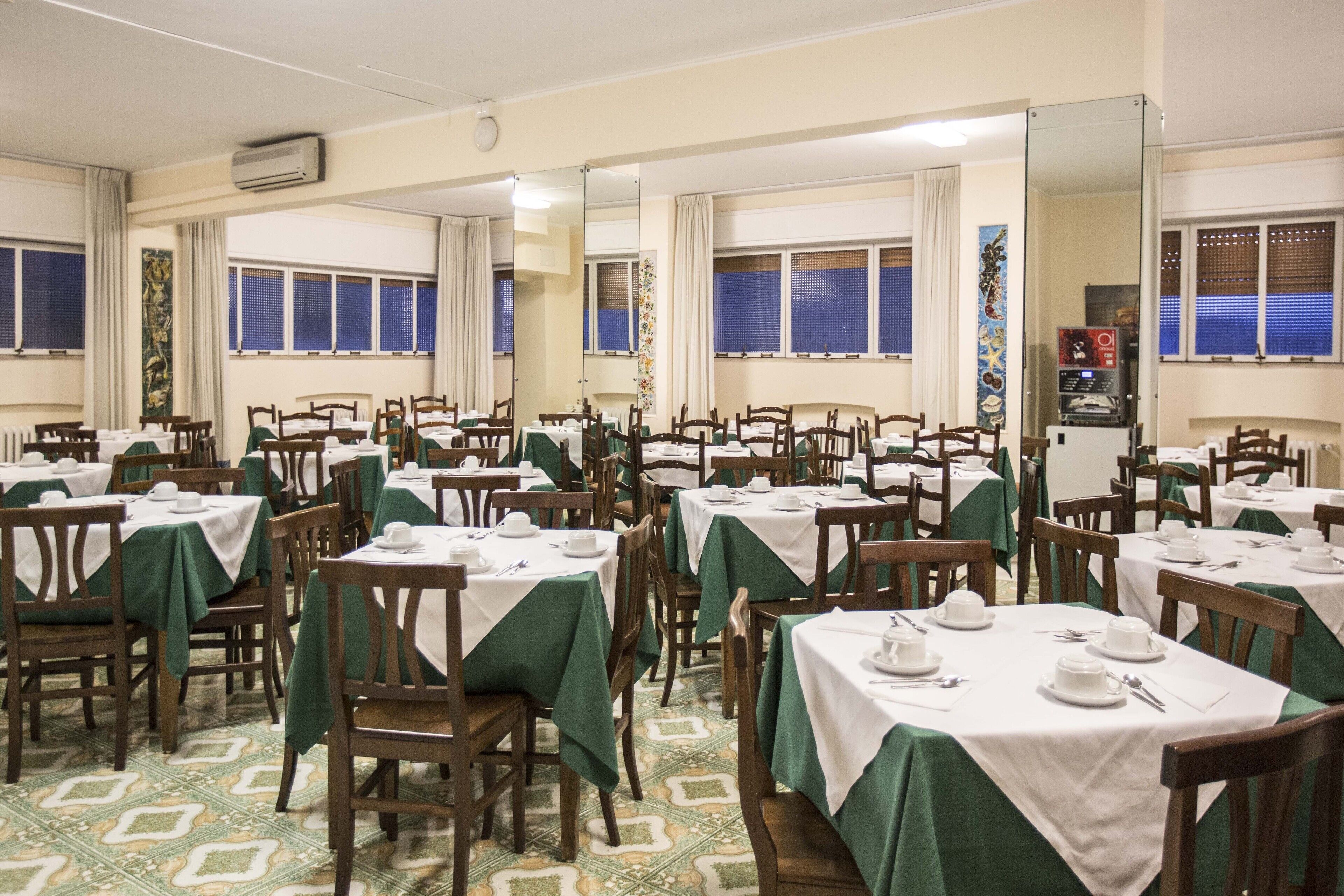 A dining area with multiple tables and chairs, each set with white tablecloths and green chair covers.