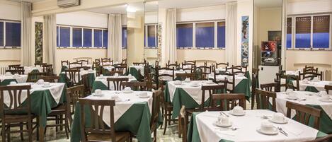 A dining area with multiple tables and chairs, each set with white tablecloths and green chair covers.