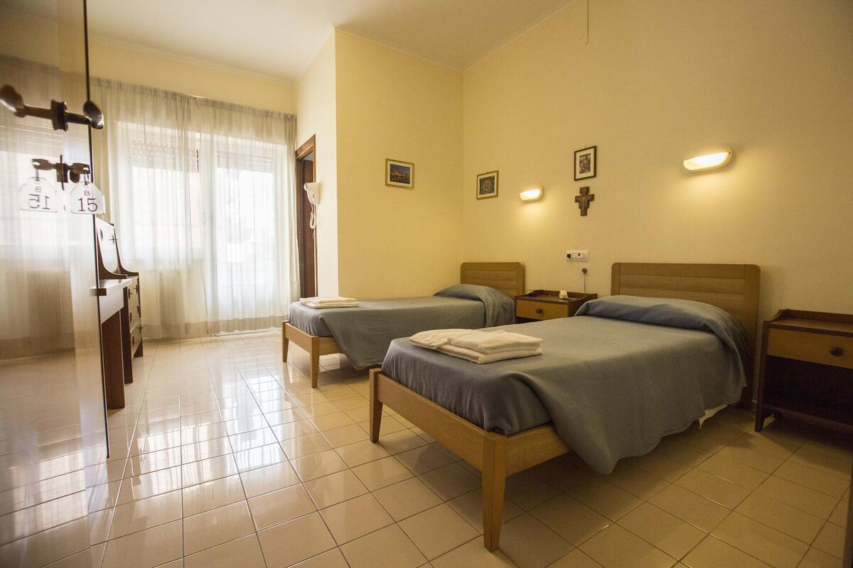 Een hotelkamer met twee eenpersoonsbedden, een houten nachtkastje, een bureau en een stoel.