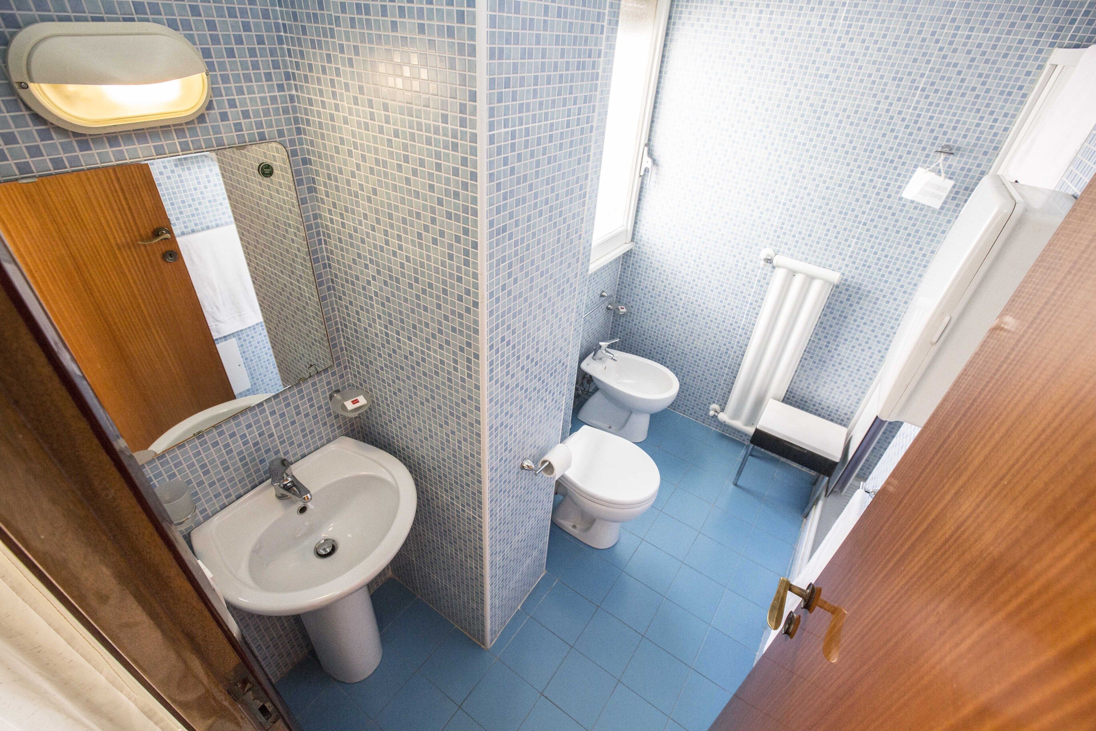 A compact bathroom with a sink, two toilets, a mirror, and a shower area.