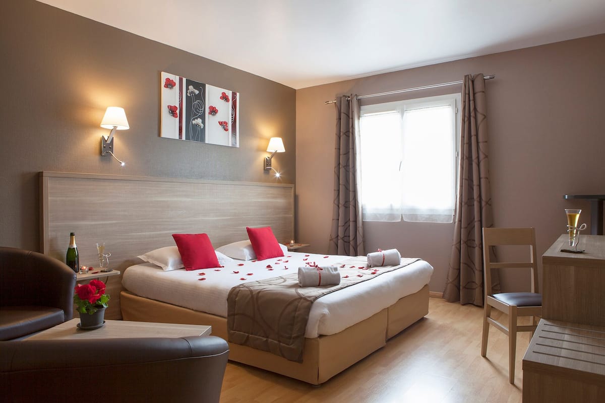 A hotel room with a bed, bedside tables, a desk, a chair, and a window with curtains.