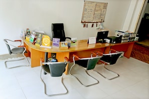 A reception desk with a glass top, surrounded by metal chairs with wooden armrests. A whiteboard with handwritten notes is on the wall behind the desk. - Hang Tep Hostel (Siem Reap)