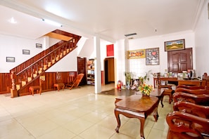 A spacious lobby with a wooden staircase, a dining area with wooden furniture, and a wall with framed pictures. - Hang Tep Hostel (Siem Reap)