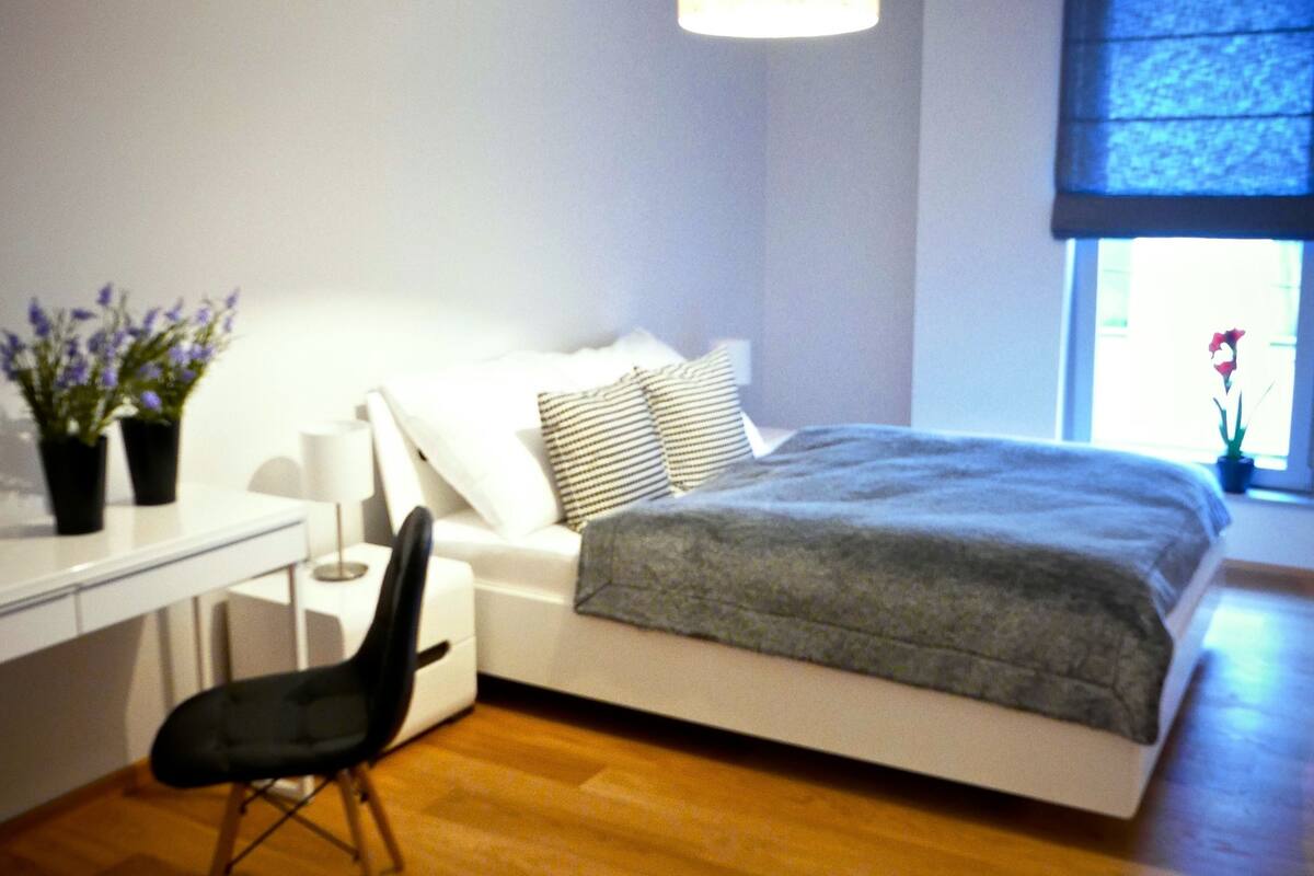 A modern bedroom with a bed, bedside table, chair, and a desk.