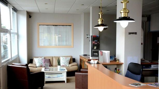 A modern office with a reception desk, a sofa, and a coffee table. - Hôtel le Petit Trianon (Saint-Brevin-les-Pins)