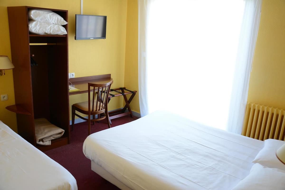 Ein Hotelzimmer mit zwei Betten, einem Schreibtisch mit Stuhl, einem Fernseher und einem Kleiderschrank.