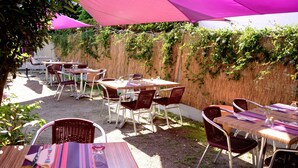 An outdoor patio area with tables and chairs, covered by a large pink canopy. - Hôtel le Petit Trianon (Saint-Brevin-les-Pins)