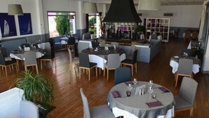 A restaurant with round tables, chairs, and a large black ceiling light. - Hôtel le Petit Trianon (Saint-Brevin-les-Pins)