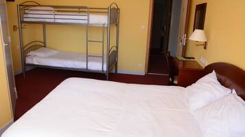 A room with a bunk bed, a single bed, a wooden nightstand with a lamp, and a door leading to another room.