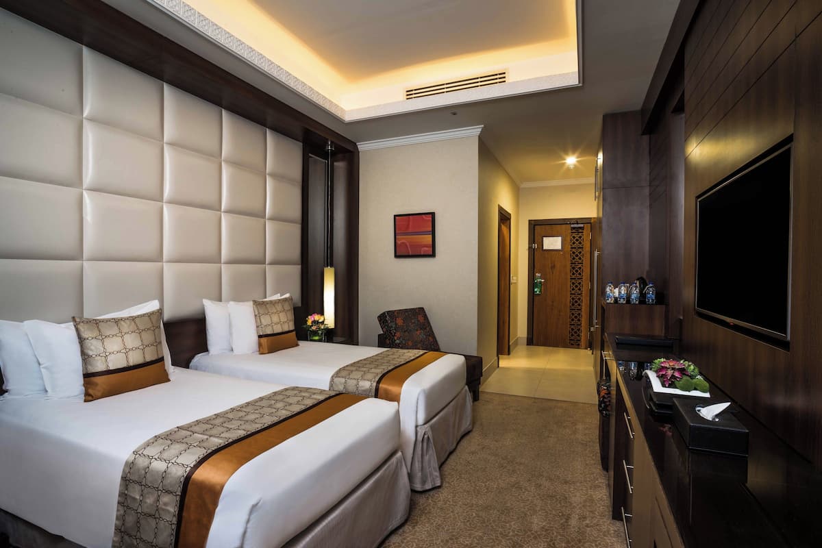 Habitación de hotel con dos camas, un televisor y un escritorio con un florero.