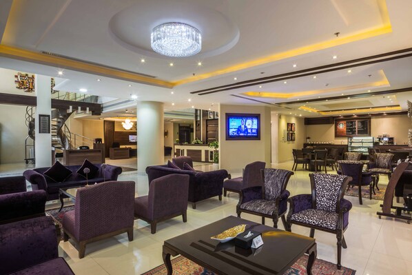 A spacious lobby with purple upholstered seating, a chandelier, and a television displaying news.