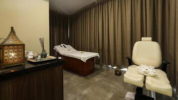 Relax in a serene spa room with a massage table, wooden foot bath, and comfortable seating area.