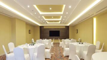 Un salón de conferencias con sillas y mesas blancas, una pantalla grande e iluminación empotrada.