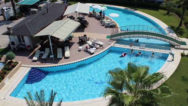 Una gran piscina con un puente, sillas de descanso y una zona de estar cubierta.