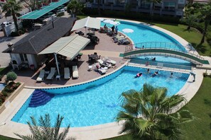 A large swimming pool with a bridge, lounge chairs, and a covered seating area. - Tebriz Apart Hotel (Kemer)