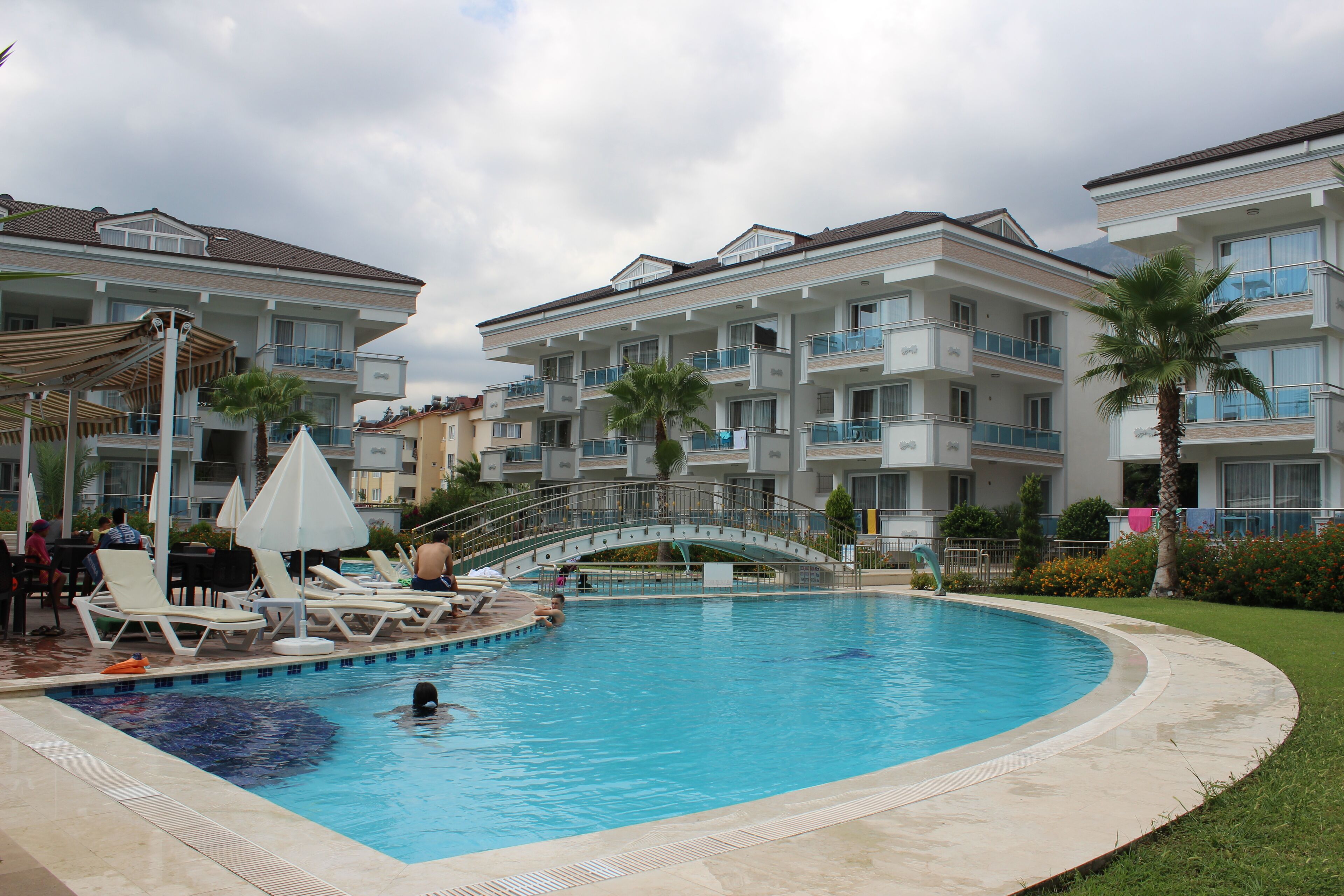 Una piscina con lettini e ombrelloni, circondata da edifici a più piani con balconi.
