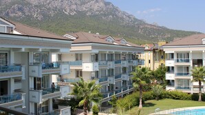 Un hotel con varios balcones, piscina y montañas al fondo.