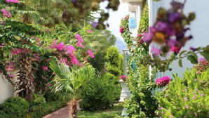 Un jardín con camino de ladrillo, abundante vegetación y plantas en flor.