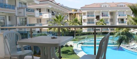 Un balcón con mesa y sillas que da a una piscina y un paisaje montañoso.