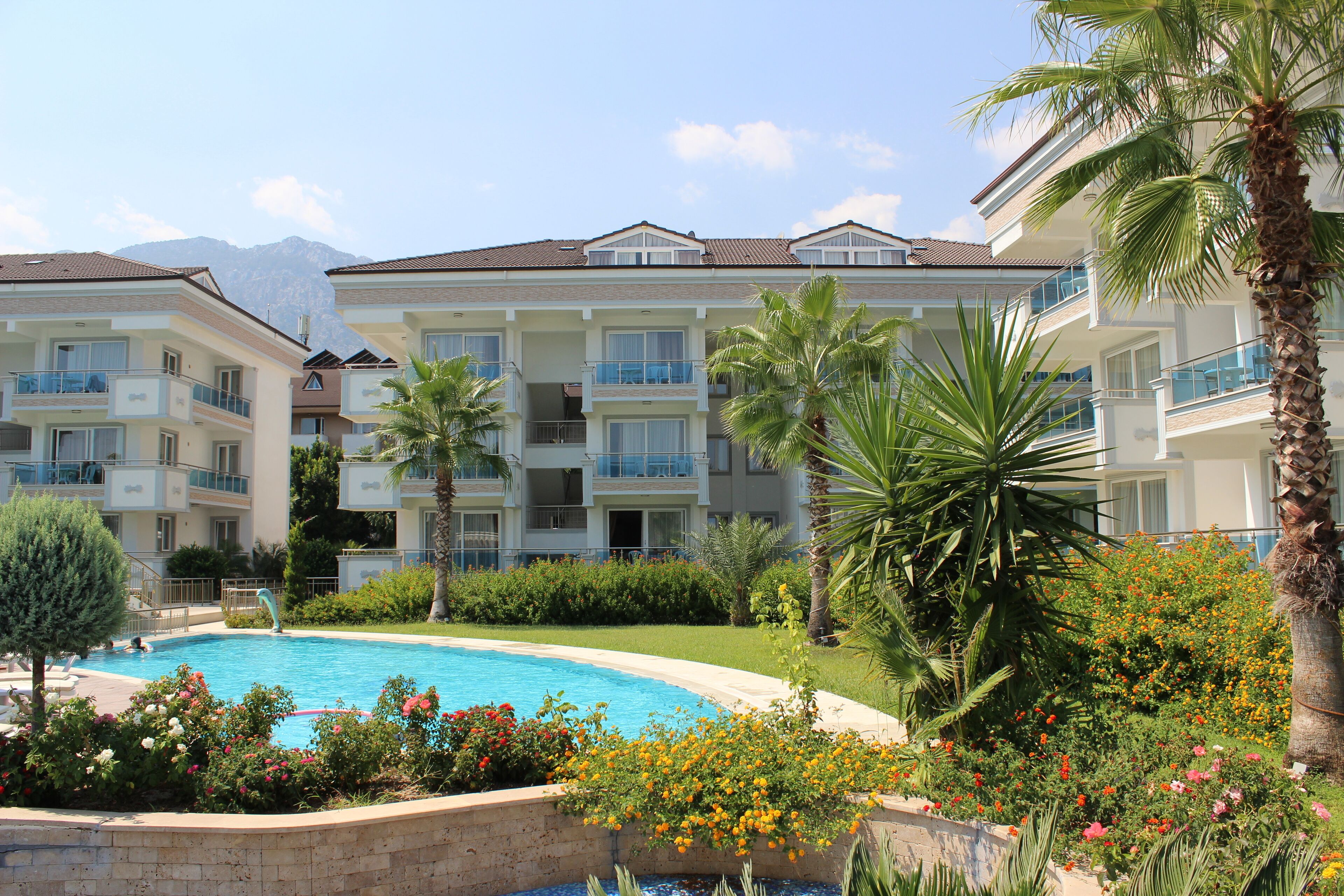 A hotel with multiple balconies, a swimming pool, and lush greenery.
