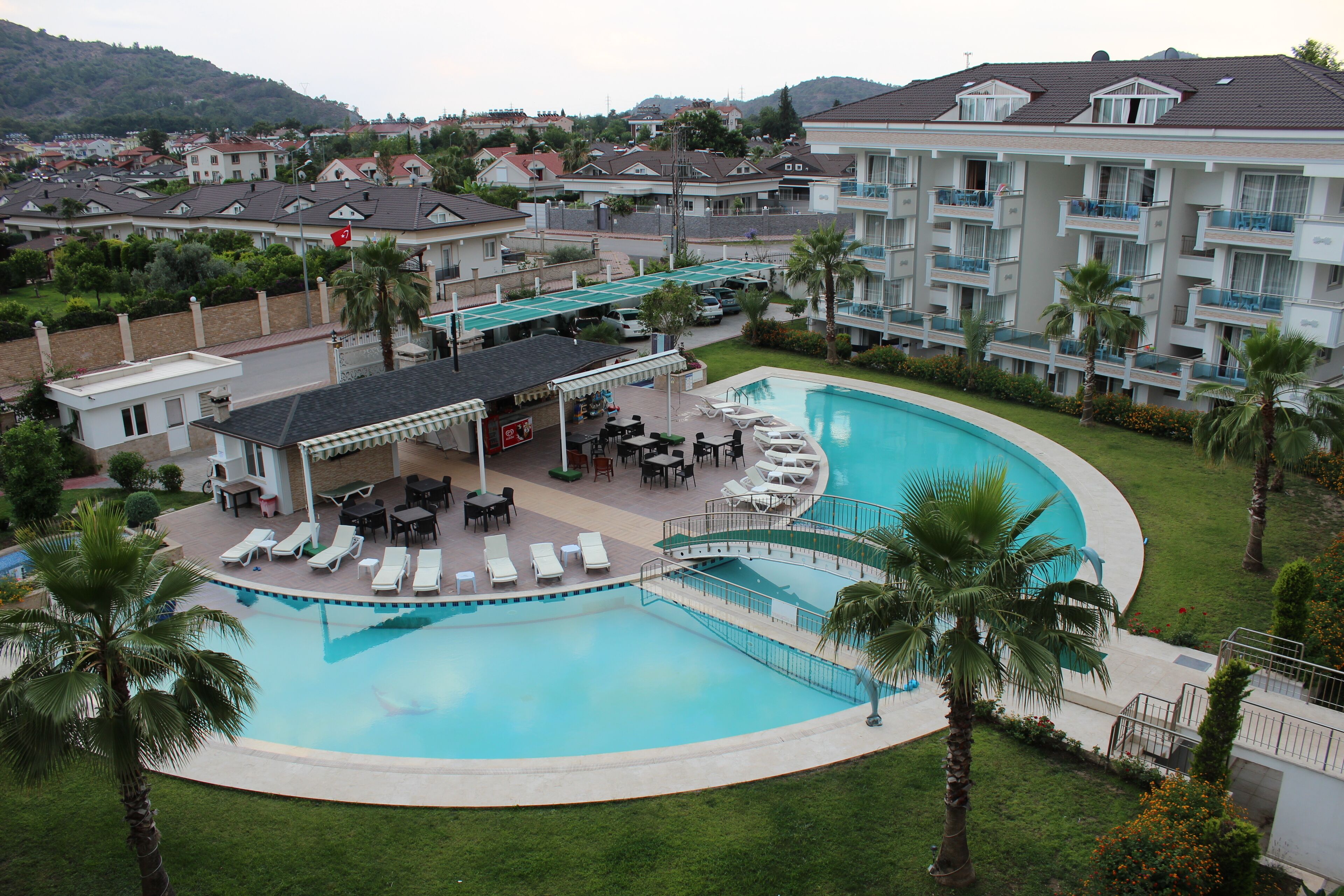 A resort with a large swimming pool, lounge chairs, and a covered area with tables and umbrellas.