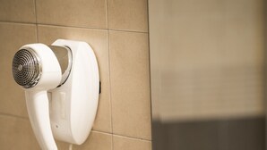 A bathroom with a hair dryer mounted on the wall, a towel rack, and a sink with toiletries. - Hotel Corte Business (Cavriago)