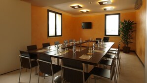 A conference room with a long table, chairs, a television, and a potted plant. - Hotel Corte Business (Cavriago)