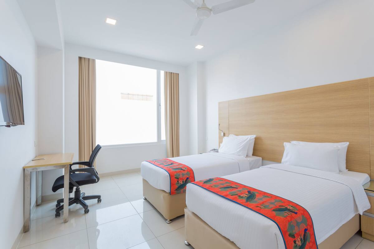 A hotel room with two beds, a desk, and a chair.