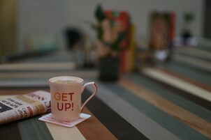 A pink mug with "GET UP!" on a wooden table with newspapers and a coaster.
