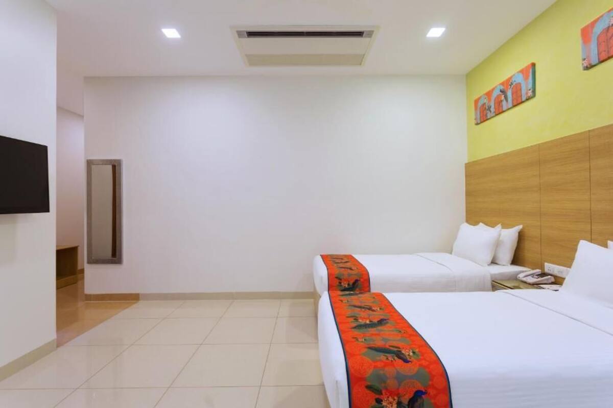 A hotel room with two beds, a flat-screen TV, a wooden headboard, and a door.