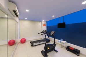 A fitness room with a treadmill, elliptical, red exercise balls, and a water station. - GINGER Noida City Center (Noida)