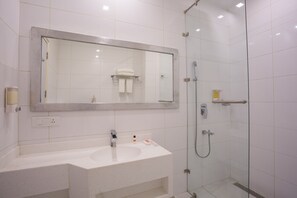 A modern bathroom with a large mirror, a sink, and a glass-enclosed shower. - GINGER Noida City Center (Noida)