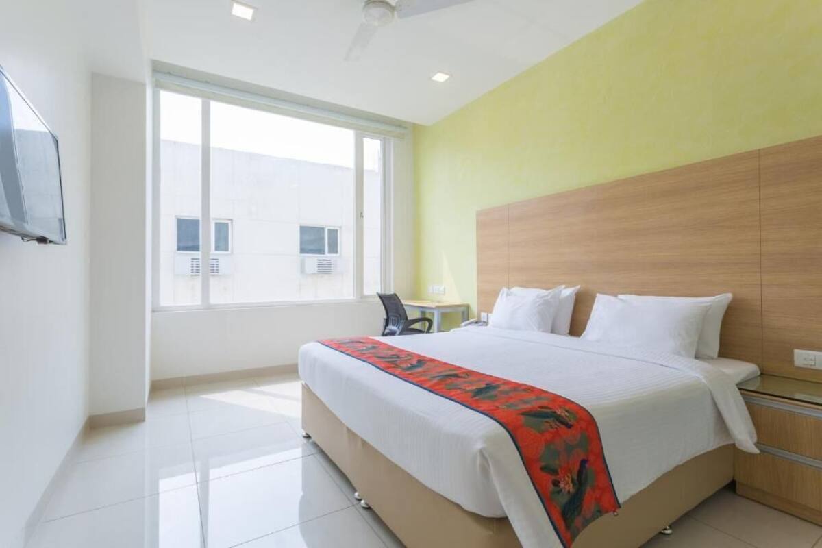 A hotel room with a bed, a desk, a chair, a window, and a television.