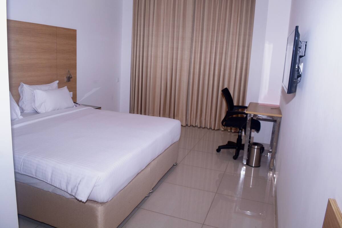 A hotel room with a bed, a desk, a chair, a TV, and a curtain.