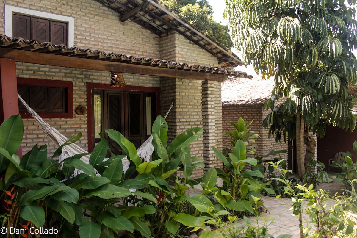 A brick house with a tiled roof, a hammock, and lush greenery.