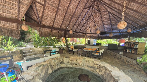 Un área de estar al aire libre con techo de paja, paredes de piedra, una pequeña piscina y una chimenea de piedra.