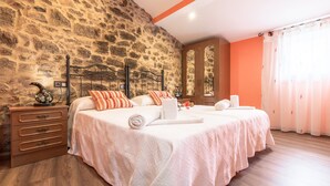 A bedroom with a stone wall, two beds with white bedding, wooden nightstands, and a large window with curtains. - Casa Carla (Palas de Rei)