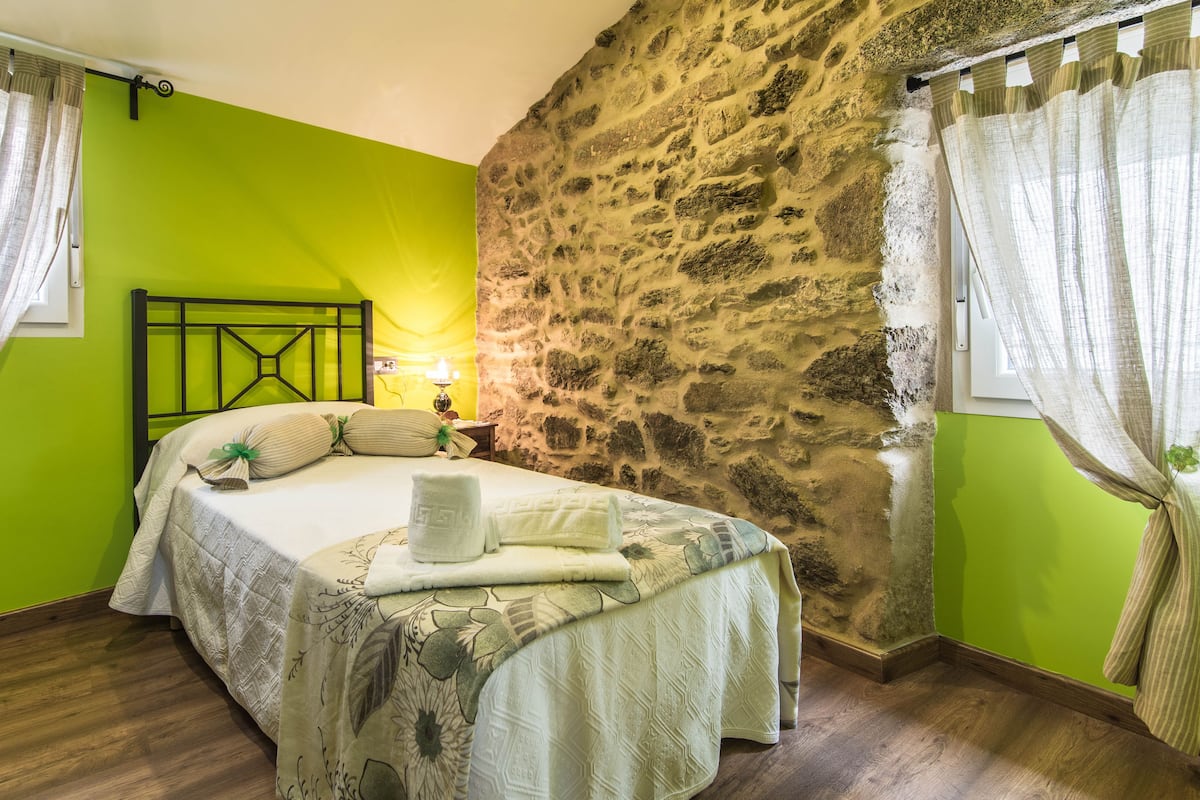 Une pièce avec un lit, un mur en pierre et une fenêtre avec des rideaux.