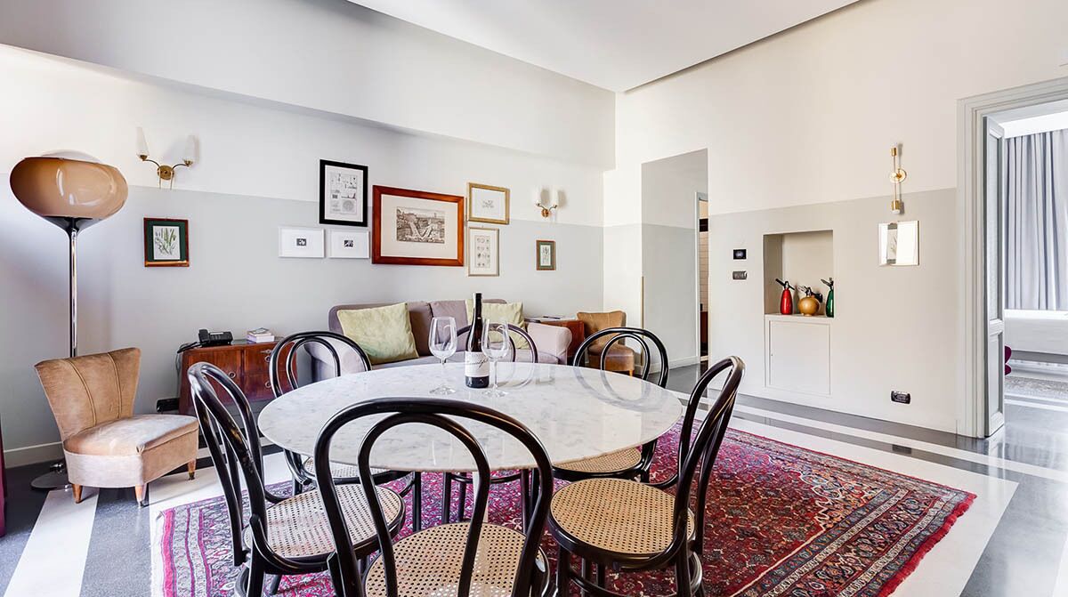A modern dining area with a round table, chairs, and a patterned rug.