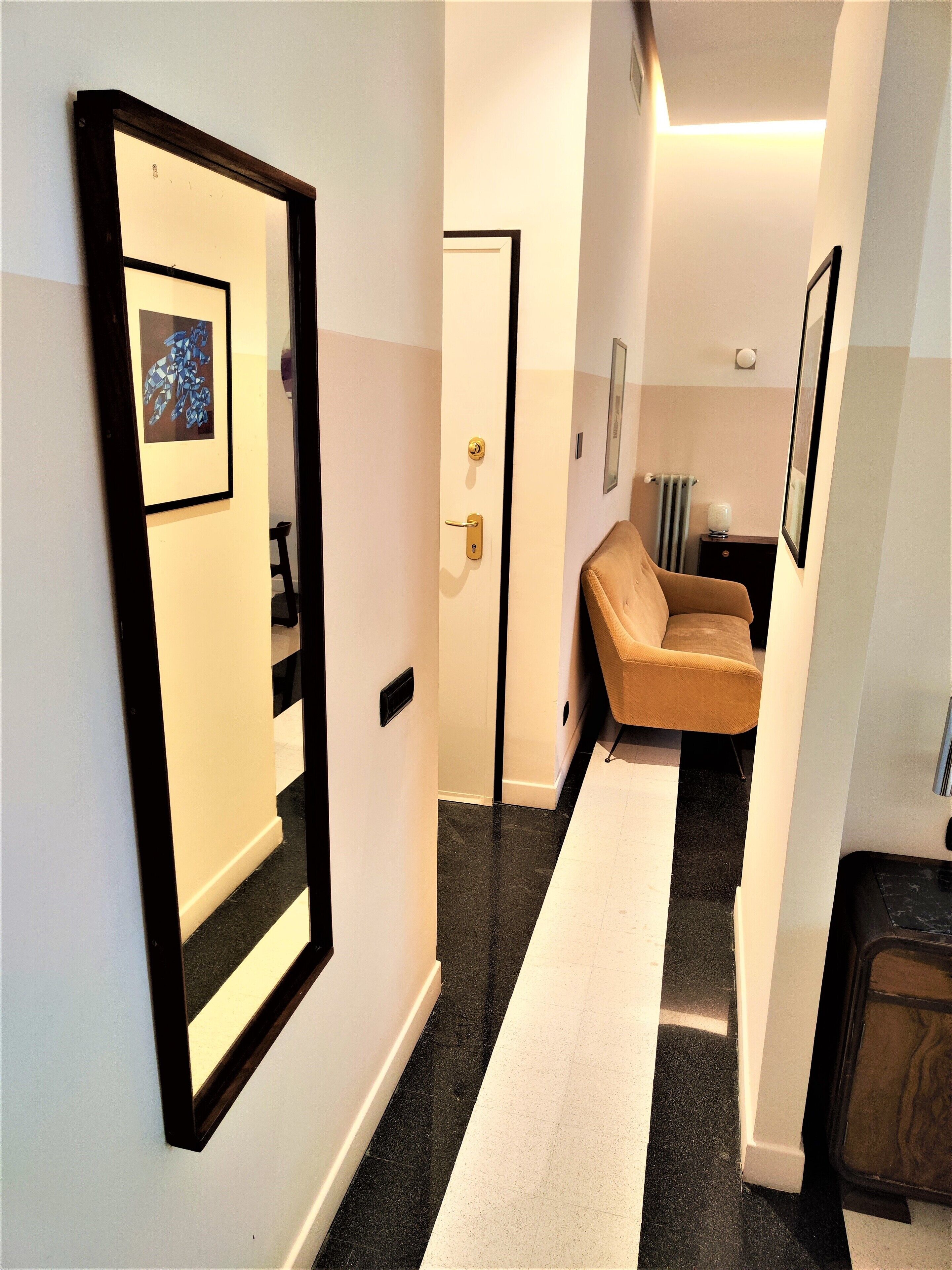 A hallway with a black and white striped floor, a beige sofa, and a framed picture on the wall.