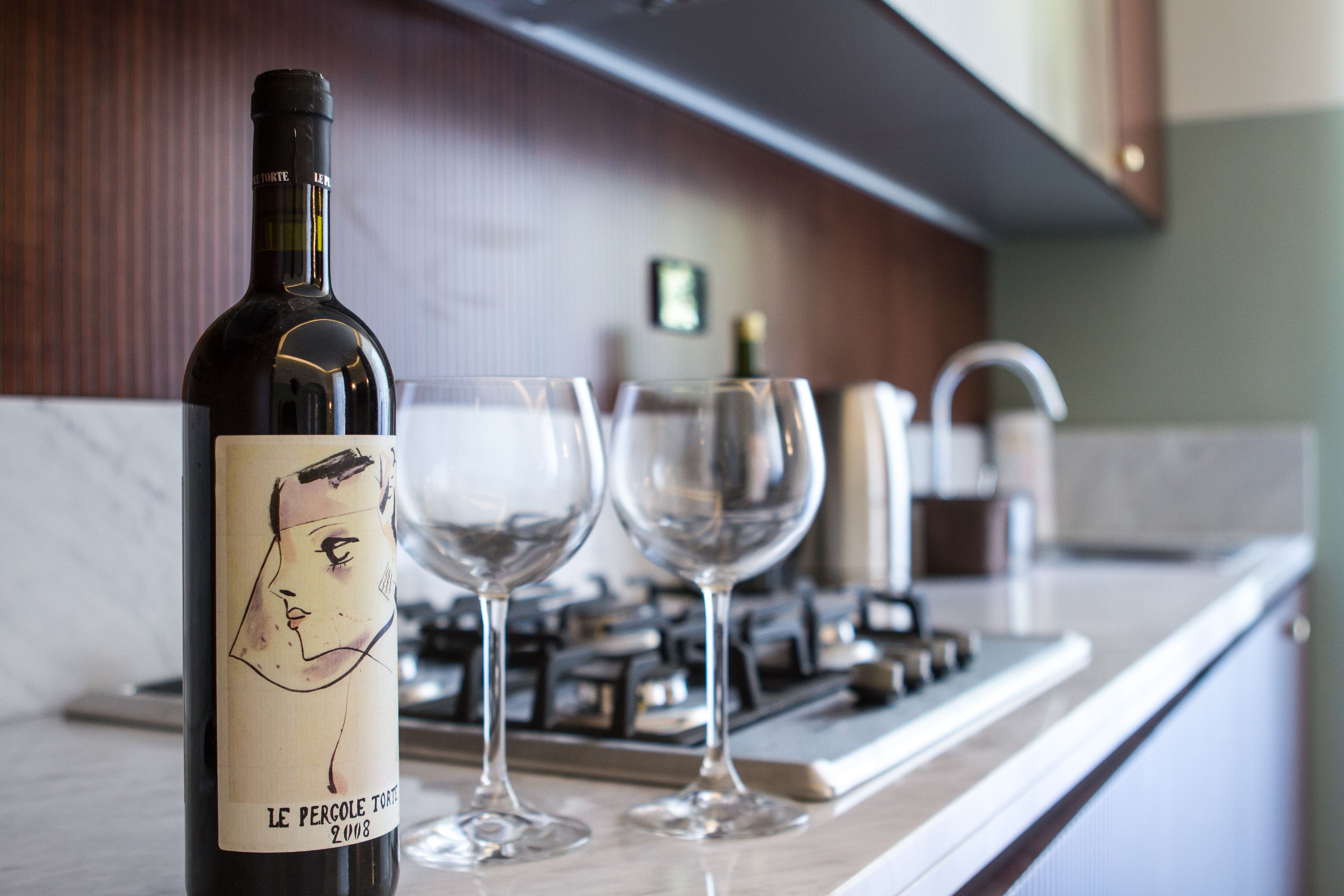 A wine bottle with a label and two empty wine glasses on a kitchen counter.