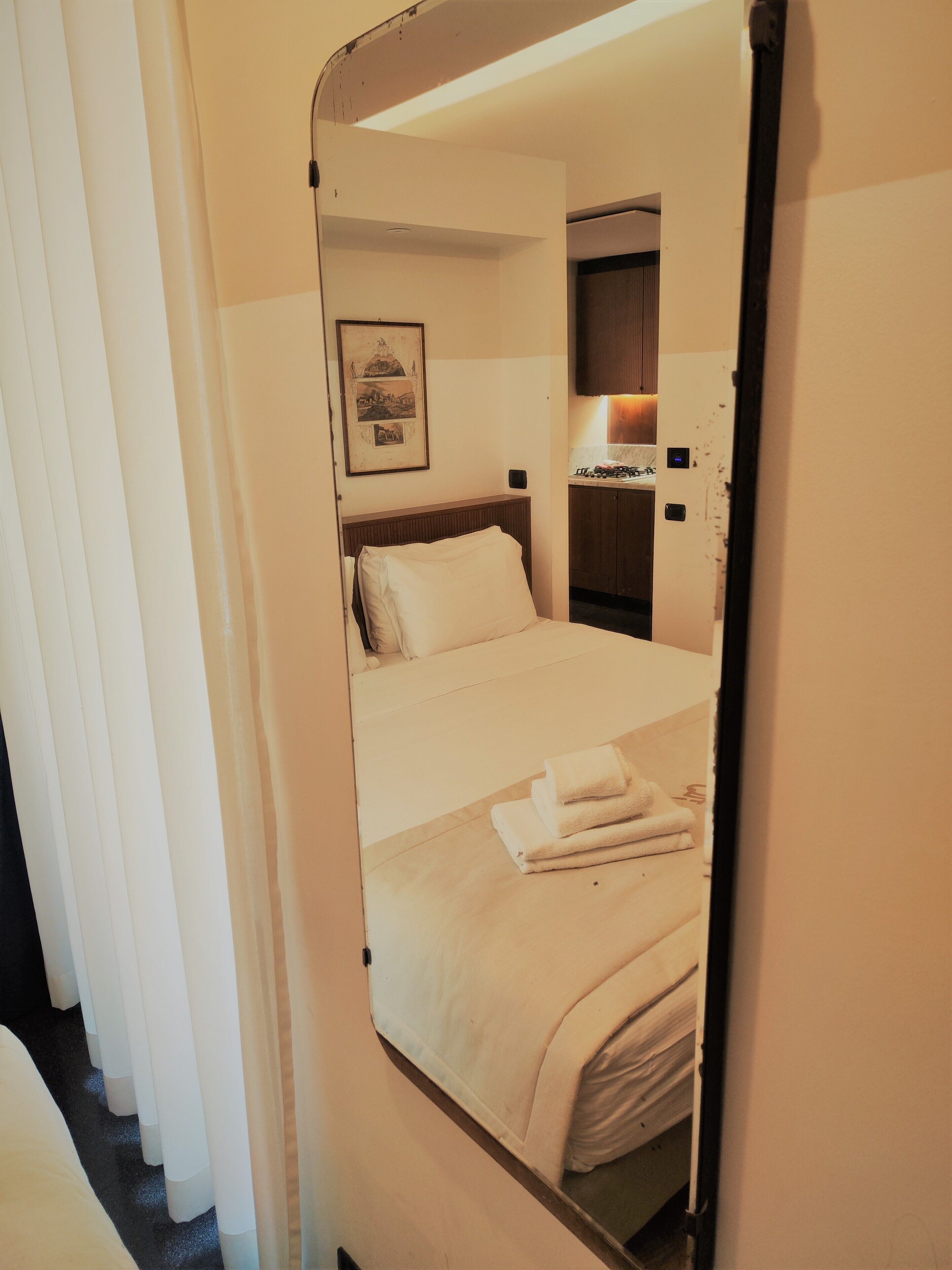 A hotel room with a bed, a bedside table, a mirror, and a framed picture on the wall.