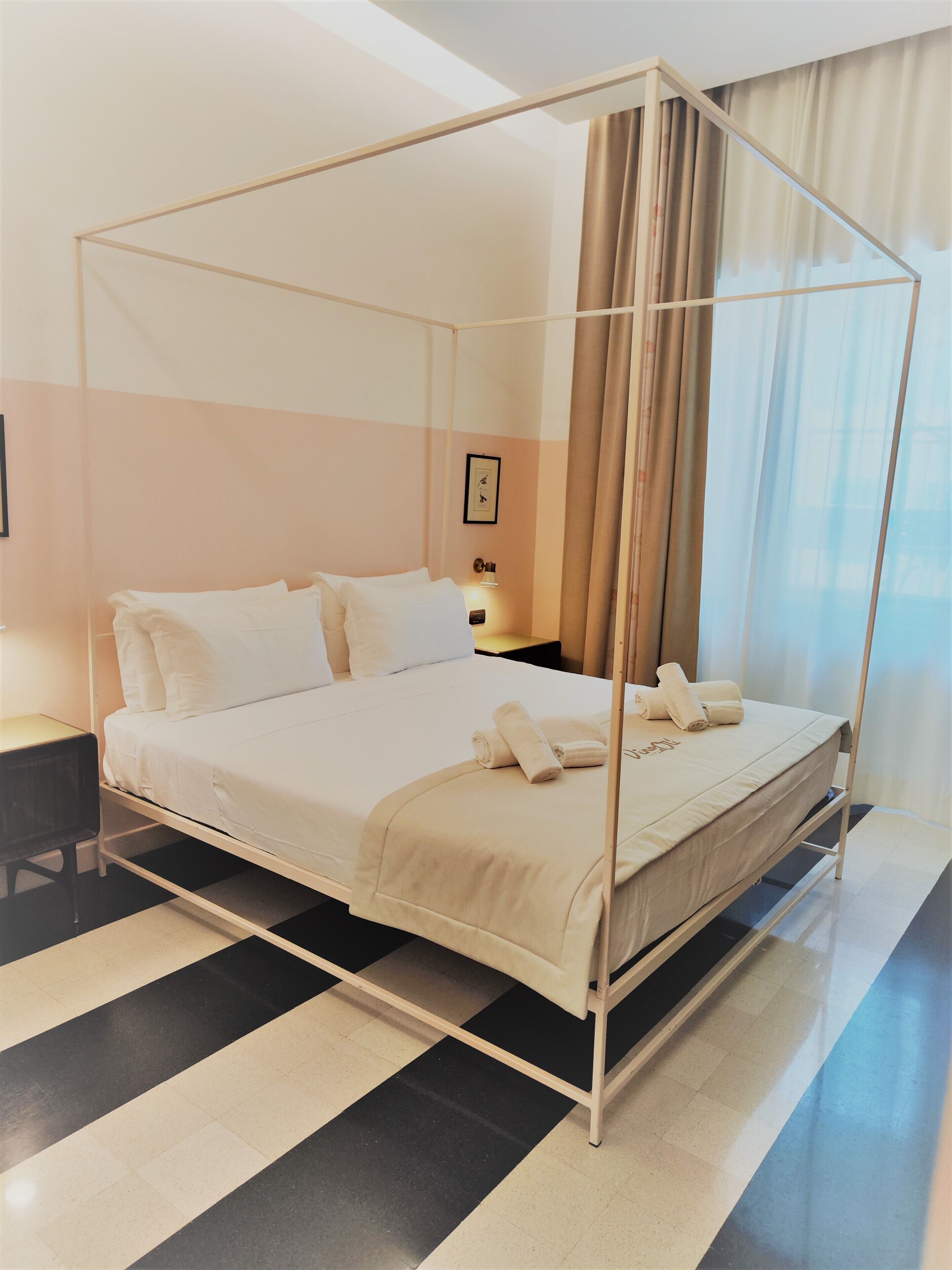 A modern hotel room with a four-poster bed, a nightstand, and a framed picture on the wall.