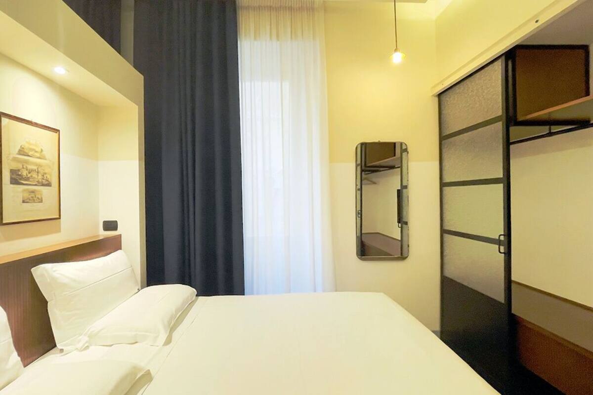 Habitación de hotel con cama, armario, espejo y un cuadro en la pared.