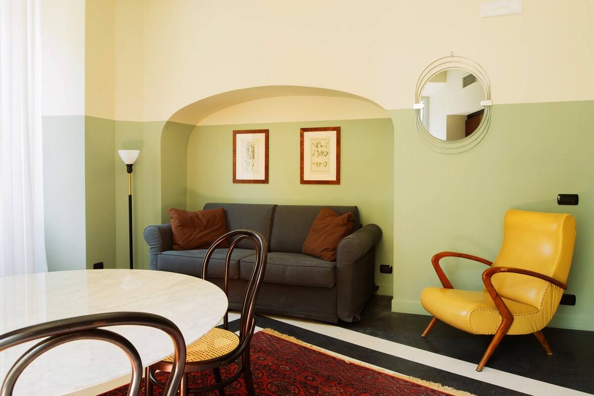 Una sala de estar con una mesa redonda, un sofá, un sillón amarillo y dos cuadros en la pared.